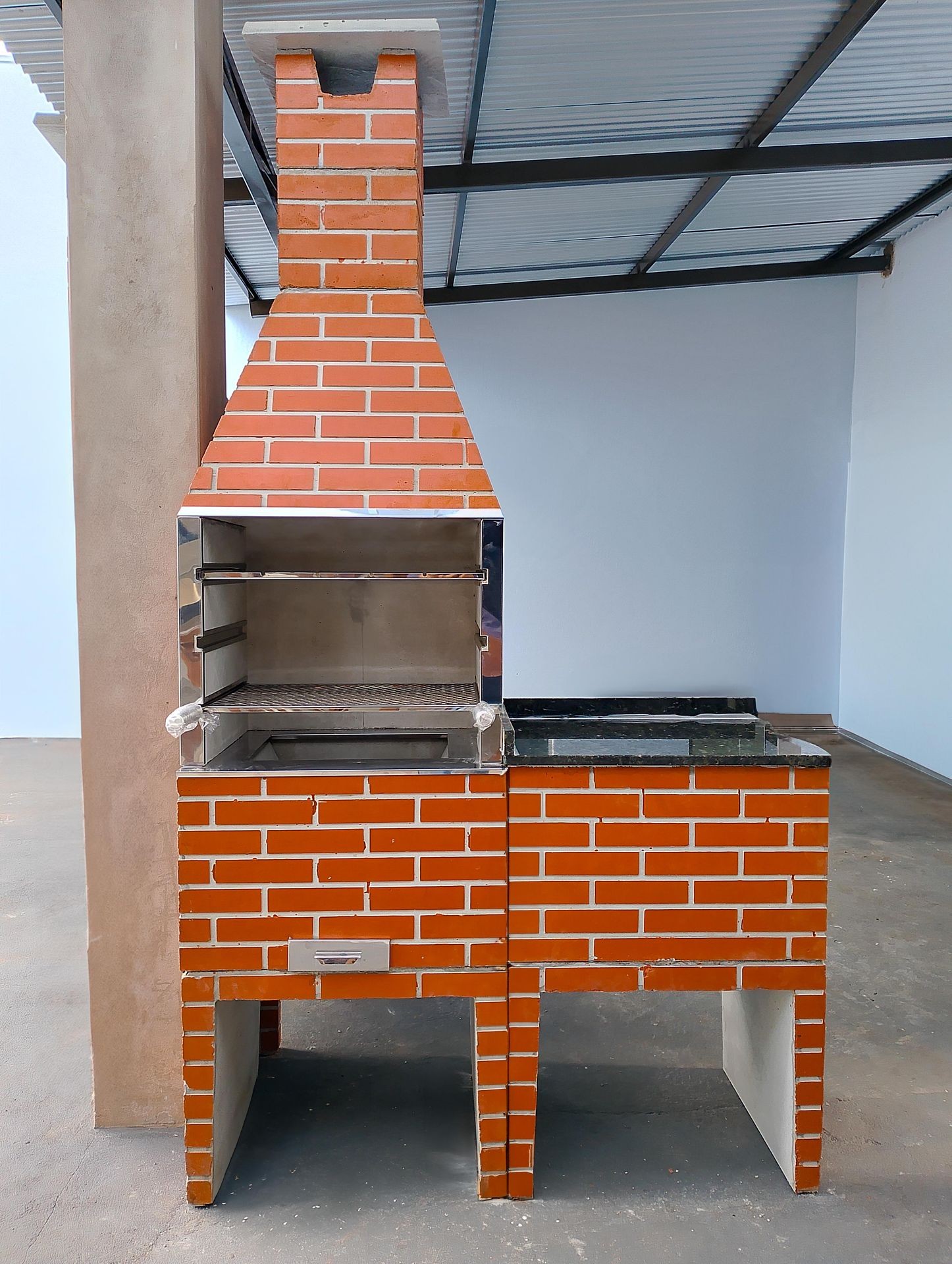 Brick barbecue grill with chimney under a metal roof.