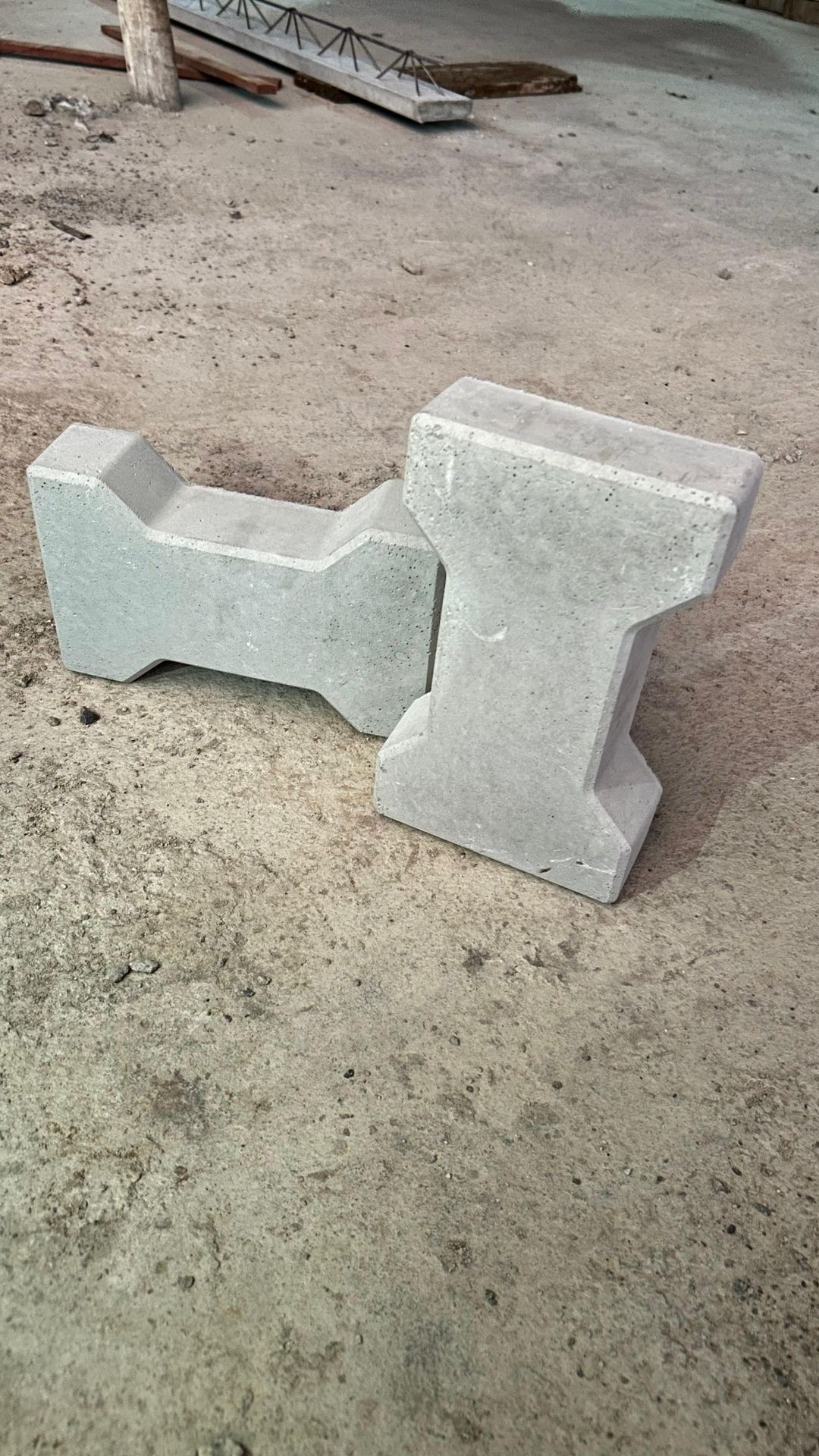 Two interlocking concrete blocks on a dusty construction site floor.